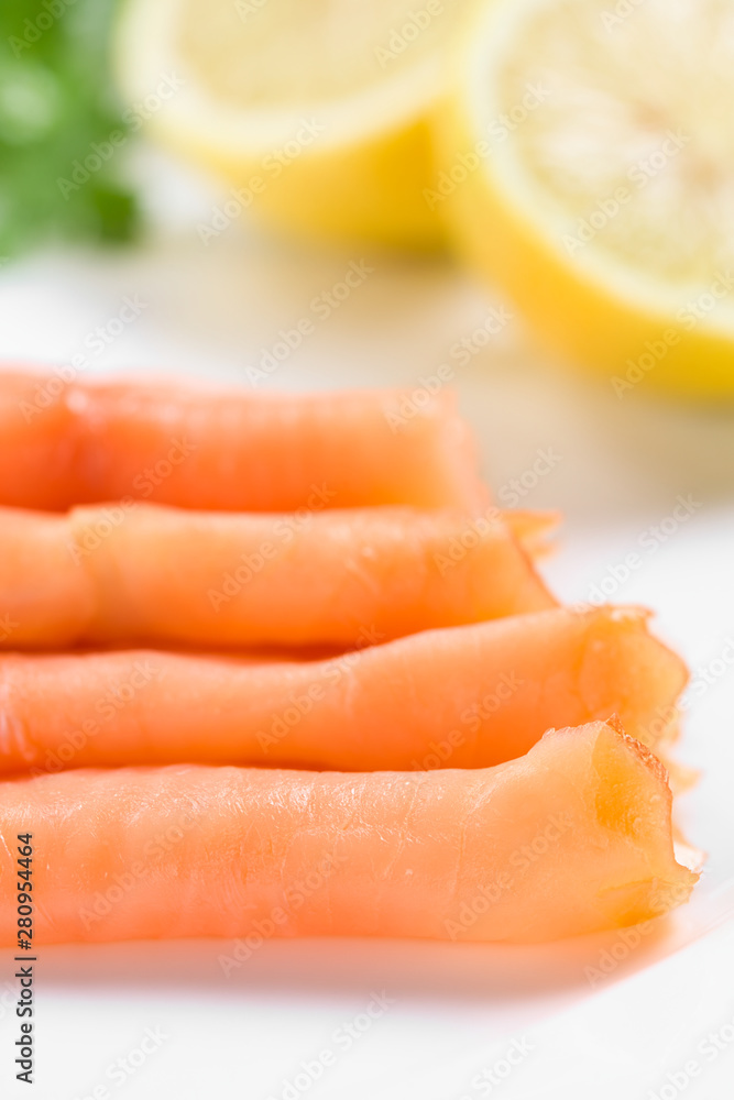 Smoked salmon slices with lemon halves on white plate (Selective Focus, Focus on the first slice)