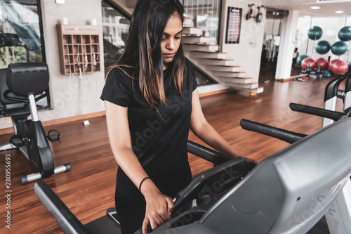 Happy fitness young lady running on treadmill machine and enjoying music from smart-phone