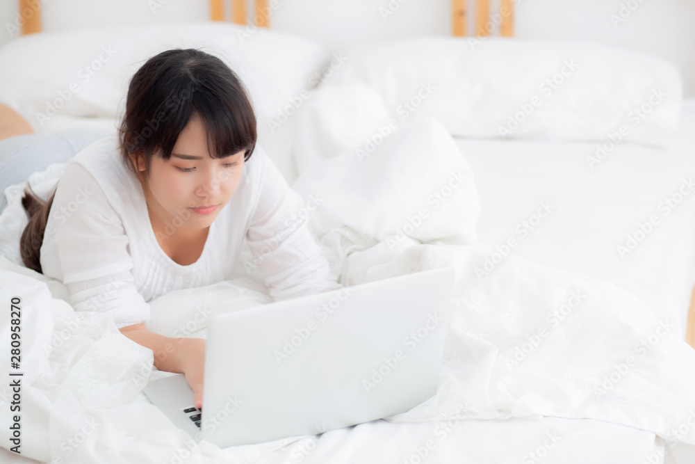 Beautiful portrait asian young woman smile lying on bed using laptop computer with happy at bedroom for leisure and relax, freelance with girl working notebook, communication concept. Beautiful portrait asian young woman smile lying on bed using laptop computer with happy at bedroom for leisure and relax, freelance with girl working notebook, communication concept.