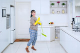 Pretty housekeeper dancing with a broom in kitchen