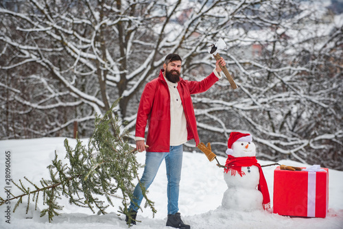 A handsome young man with snow man carries a Christmas tree. Merry Christmas and happy new year greeting card. Snowman with gift.