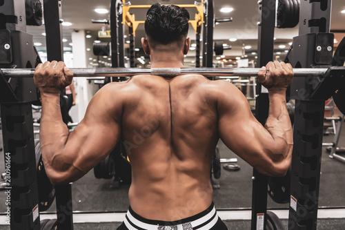 Man at the gym. Execute exercise squatting with weight, in gym