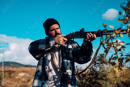 Bearded hunter man holding gun and walking in forest. Hunter with shotgun gun on hunt. Big game.