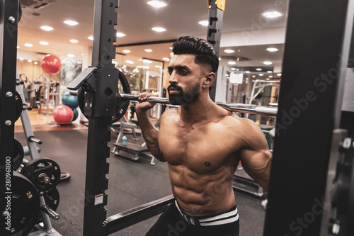 Man at the gym. Execute exercise squatting with weight, in gym