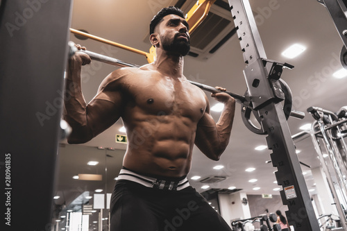 Man at the gym. Execute exercise squatting with weight, in gym