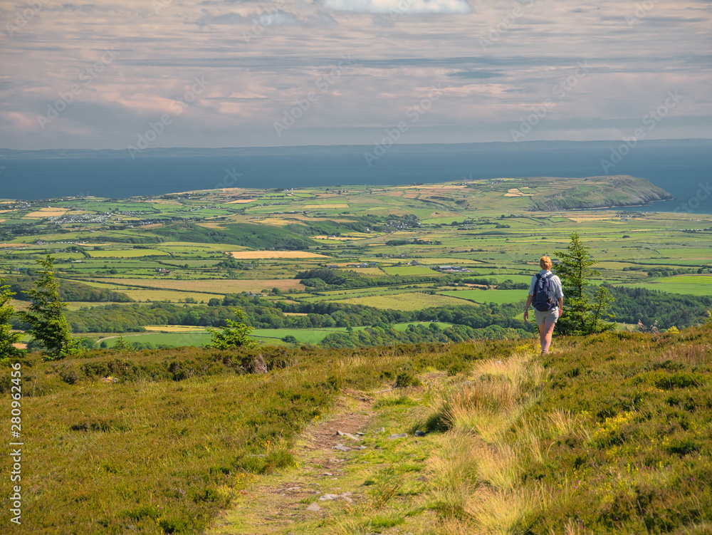 A view of the south of the Llyn Peninsula with a lone walker on the path down Garn Fadryn in Gwynedd, Wales, UK