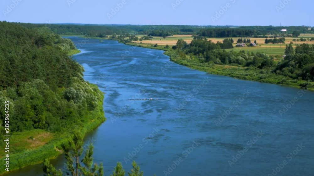 Handheld shot of wide river surrounded by green land with tree branches being blownd by light breeze. Handheld shot of wide river surrounded by green land with tree branches being blownd by light breeze.