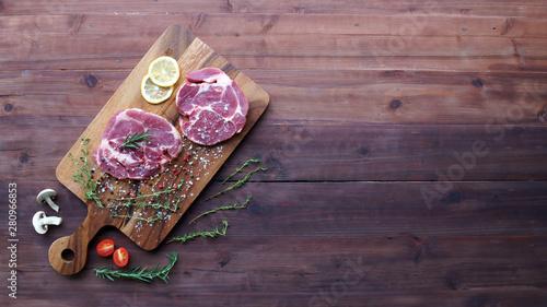 Slices of raw pork meat topped with Fresh rosemary herb on wooden board. Top view with copy space.