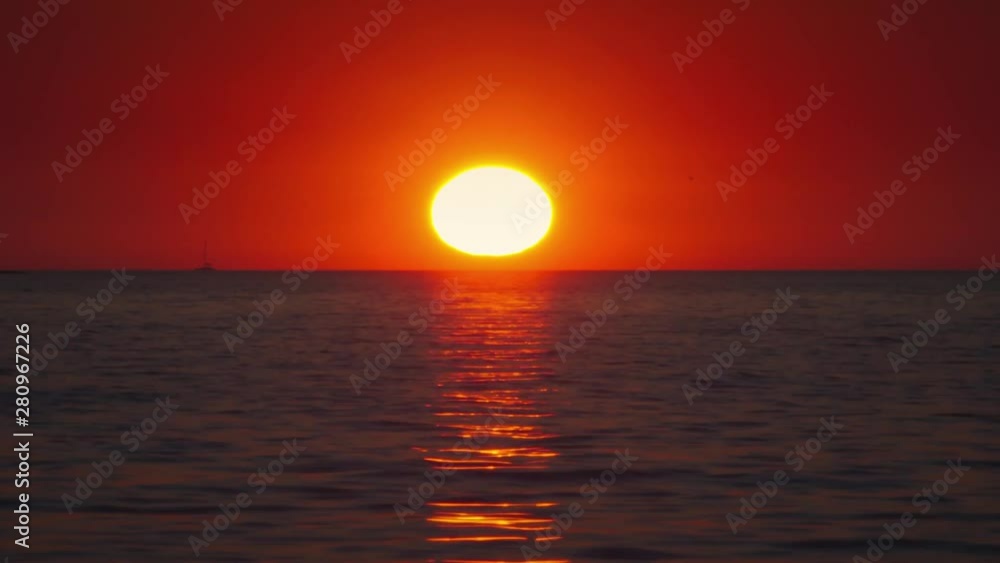 The sun is setting over the horizon at a beach at the Croatian Mediterranean seaside. The water is moving gently and continuously. The sun is setting over the horizon at a beach at the Croatian Mediterranean seaside. The water is moving gently and continuously.