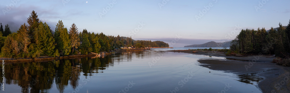 Beautiful Panoramic View of a river joining the ocean in a small town during a cloudy and sunny summer sunrise. Taken at Port Renfrew, Vancouver Island, BC, Canada.