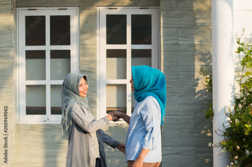 two hijab women neighbors meet and say hi while smiling and shake hands in front of their house two hijab women neighbors meet and say hi while smiling and shake hands in front of their house
