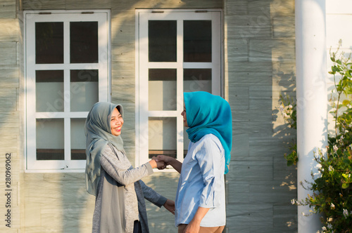two hijab women neighbors meet and say hi while smiling and shake hands in front of their house