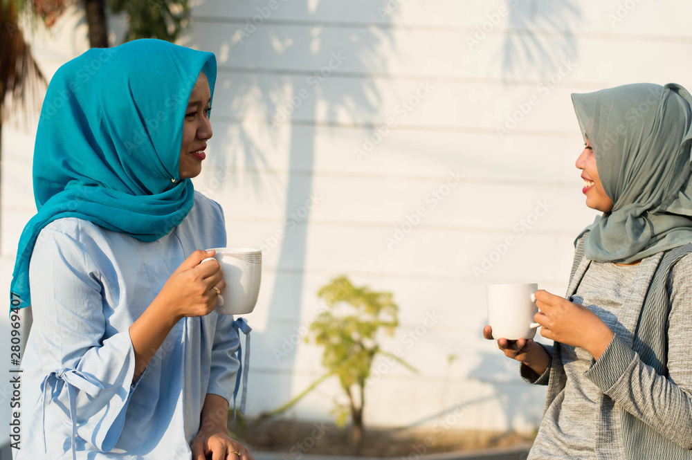 close up happy shot two hijab women drinking tea and coffee in front of the house and smiling close up happy shot two hijab women drinking tea and coffee in front of the house and smiling