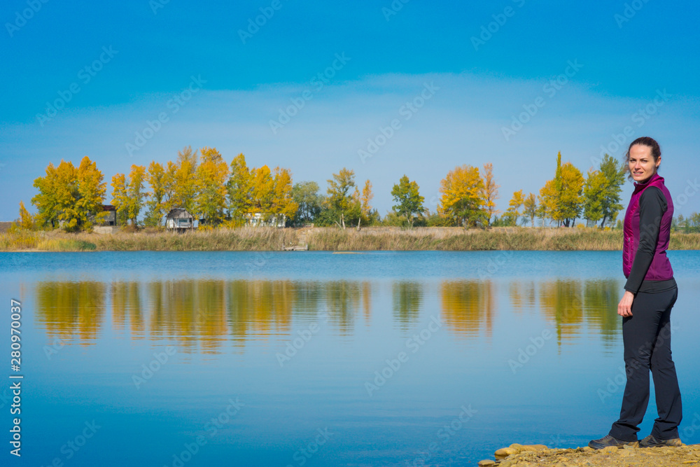 Beautiful young woman enjoying autumn by the side of a wild lake