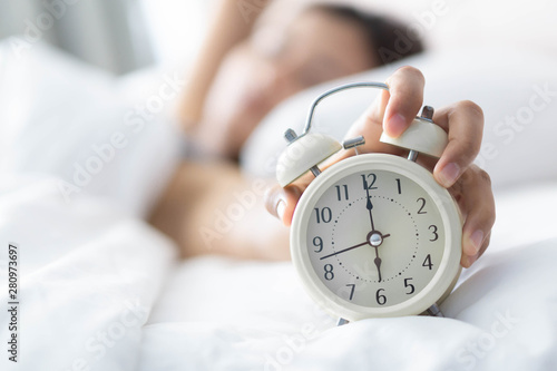 Closeup woman sleeping on bed and hand holding alarm on clock, Time to wake up