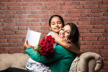Mother's Day - Indian girl / mother celebrating Mother's day with Rose Flower Bouquet, greeting card while hugging and kissing each other