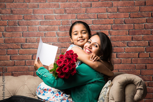 Mother's Day - Indian girl / mother celebrating Mother's day with Rose Flower Bouquet, greeting card while hugging and kissing each other photo