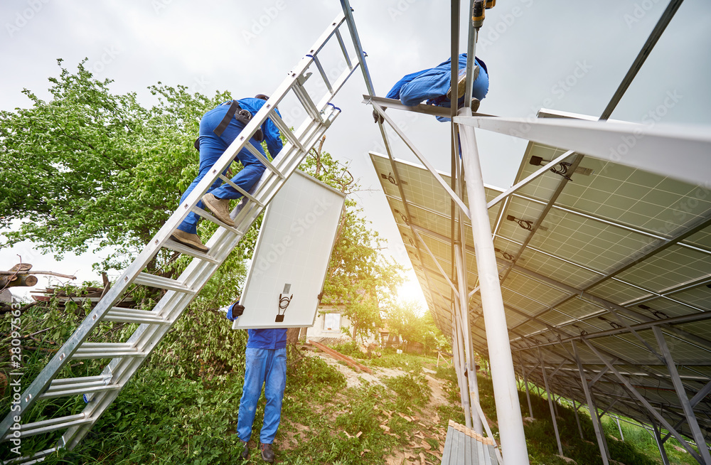 Team of three technicians mounting photo voltaic panel to stand-alone solar system platform on bright sunny day. Alternative energy, professionally done job and financial investment concept. Team of three technicians mounting photo voltaic panel to stand-alone solar system platform on bright sunny day. Alternative energy, professionally done job and financial investment concept.
