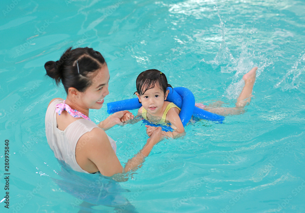Mother teaching kid in swimming pool with foam noodle