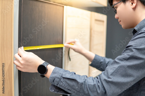 Asian man using tape measure on cabinet panel choosing materials or countertops for built-in furniture design. Shopping furniture and house decoration. Home improvement concept