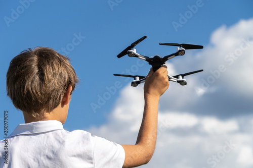 Boy playing with drone in summer day outdoors against blue sky