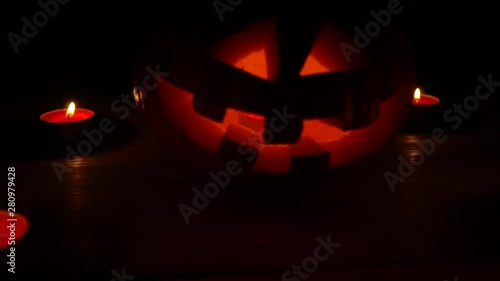 Halloween and holidays concept - spooky pumpkin lantern or carved pumpkin. Carved halloween pumpkin lights inside with a flame on a black background with candles. close-up. photo