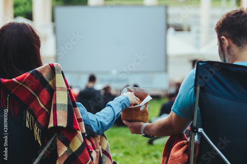 couple sitting in camp-chairs in city park looking movie outdoors at open air cinema