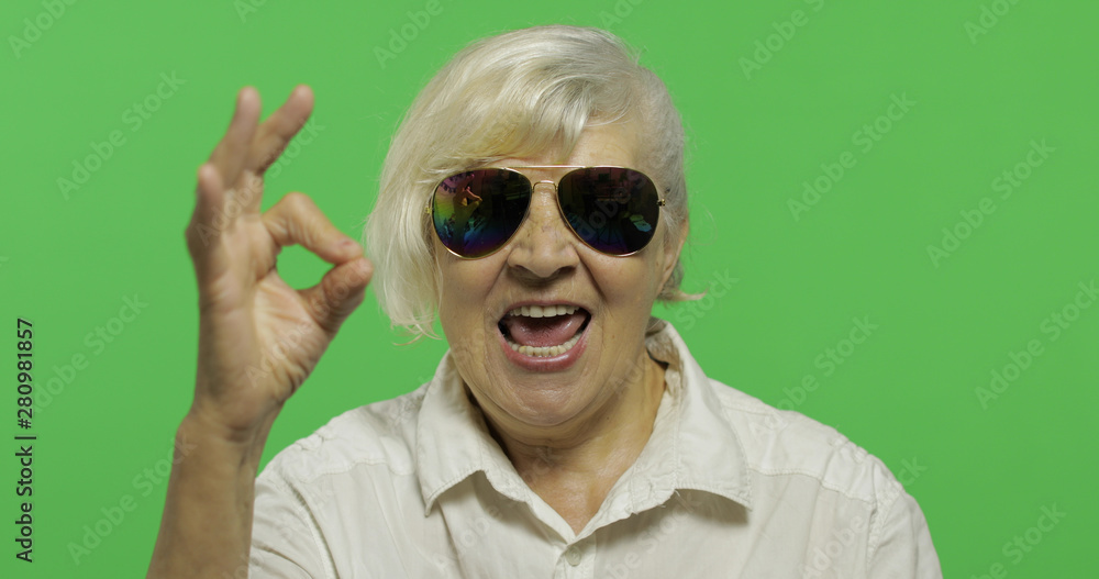 An elderly woman in sunglasses show ok gesture and smiles. Chroma key An elderly woman in sunglasses show ok gesture and smiles. Chroma key