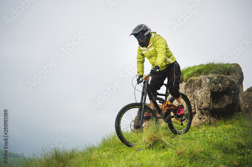 Aged male athlete in helmet and mask rides down a grassy slope on a mountain bike. Downhill mountain bike concept
