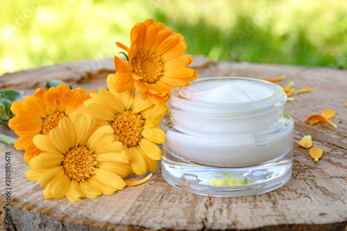 Cream for body care with calendula. Fresh orange calendula flowers on a wooden background in nature. Cosmetic cream for cleansing the skin with calendula flowers.