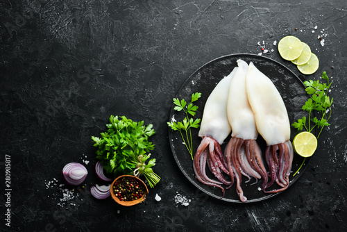 Raw squid with spices. Seafood on a black stone background. Top view. Free copy space. photo