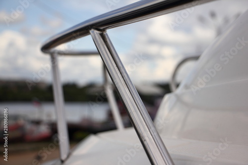 Stainless steel railing on white deck of a motor boat close-up on a blurred background of blue sky, river and yacht club - rest on the water, boating, yachting