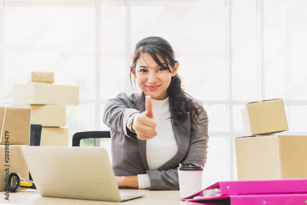 Happy successful business woman thumb up working with laptop and cardboard box on table in home office. online business success concept Happy successful business woman thumb up working with laptop and cardboard box on table in home office. online business success concept