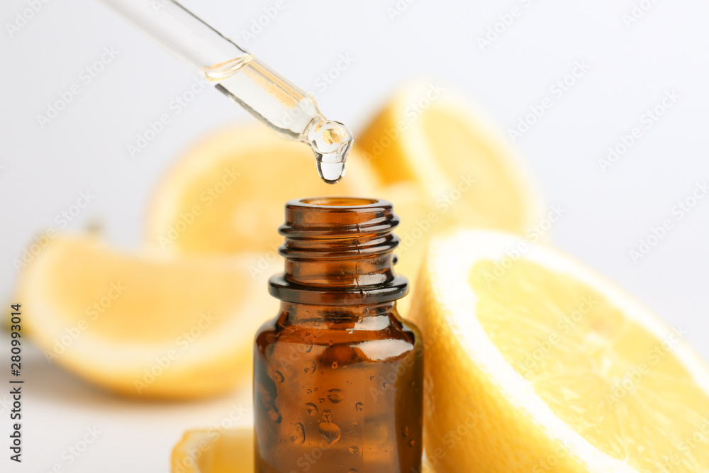 Citrus essential oil dripping from pipette into bottle on white background - obrazy, fototapety, plakaty 