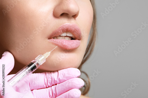 Young woman receiving injection of filler in lips, closeup photo