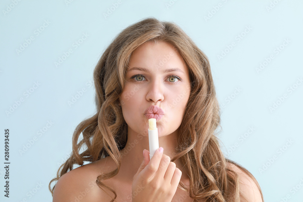 Beautiful young woman applying lipstick against color background Beautiful young woman applying lipstick against color background