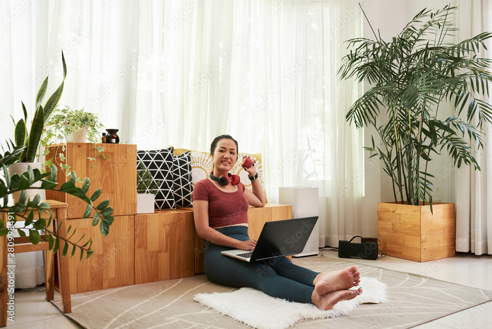 Pretty young Asian female student sitting on the floor at home with laptop, smiling and showing red apple she is having for snack Pretty young Asian female student sitting on the floor at home with laptop, smiling and showing red apple she is having for snack