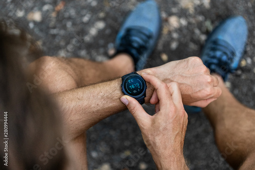 Fototapeta Naklejka Na Ścianę i Meble -  Fit man checking smart watch wearable technology sport smartwatch on fitness run walk outside. Top view from above with running shoes in street.