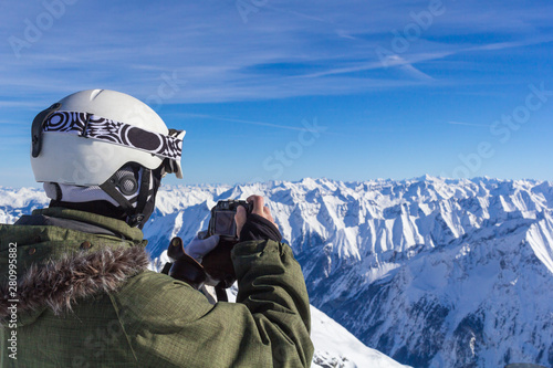 Skier man with orange ski glasses in white helmet make photoshoot on top in Alps mountains. On the background of mountains. Close up view.