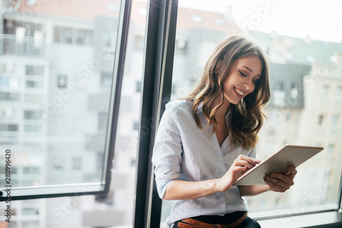 Attractive businesswoman using a digital tablet while standing in front of windows photo