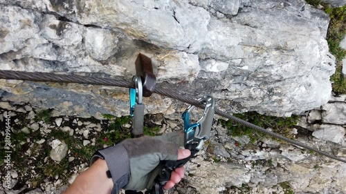 POV of via ferrata climber securing himself by placing the snap links one after another into the next segment. The climber is unsing the correct and safe technique to change the snap links. photo