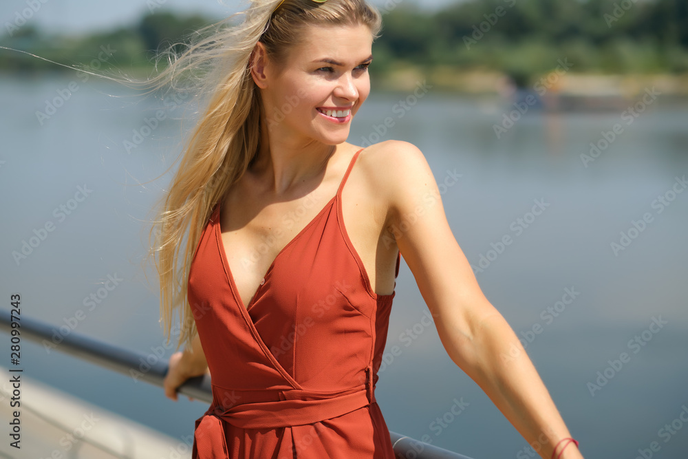 Beautiful woman in red dress. City river background.