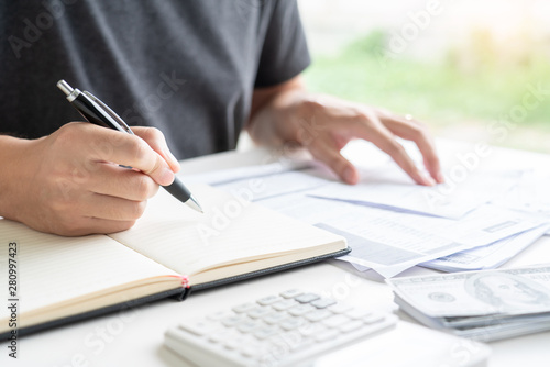 Stressed man calculating accounting holding a receipt checking bills, taxes, bank account balance counting money and making notes, check home expenses concept.