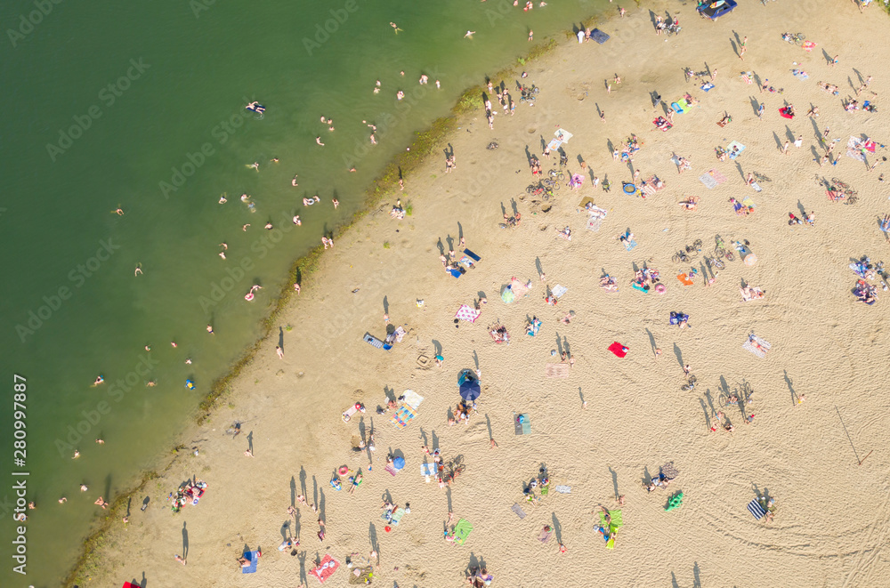 Aerial shot of city beach filled with people on hot sunny day. People relax, sunbathe and swim in pond. Aerial shot of city beach filled with people on hot sunny day. People relax, sunbathe and swim in pond.