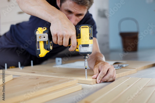 Billede på lærred Man assembling furniture at home using a cordless screwdriver