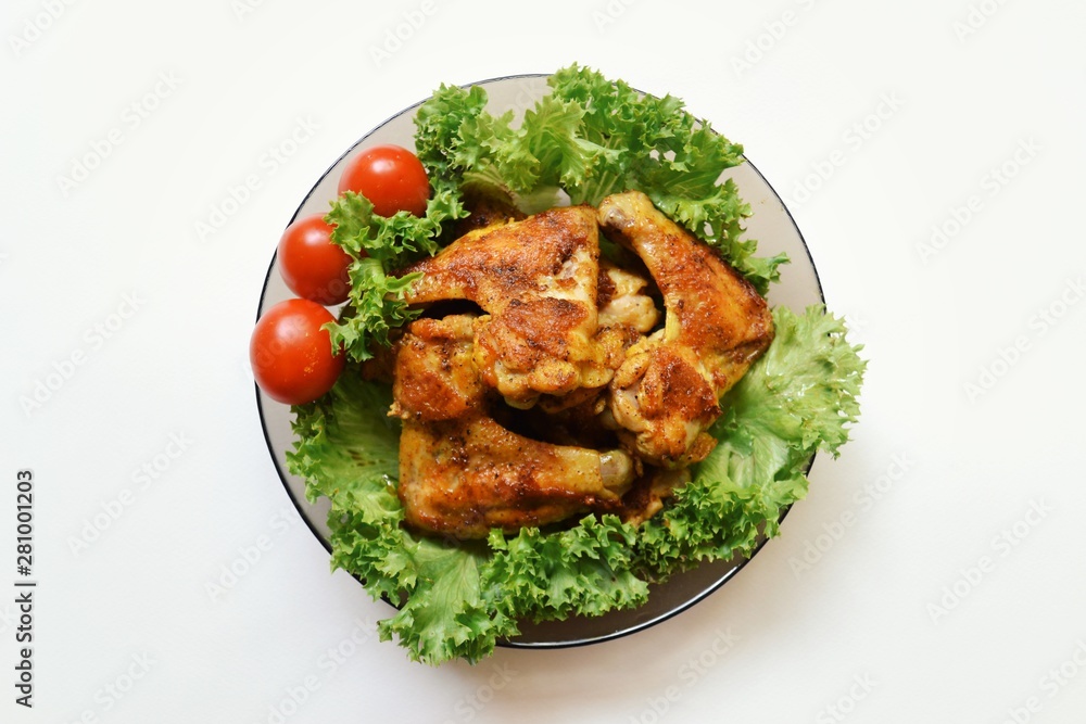 Fototapeta premium Juicy appetizing fried chicken wings in a plate isolated on white background. Grilled meat with lettuce and tomato.