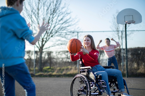 Fototapeta Naklejka Na Ścianę i Meble -  Teenage Girl In Wheelchair Playing Basketball With Friends