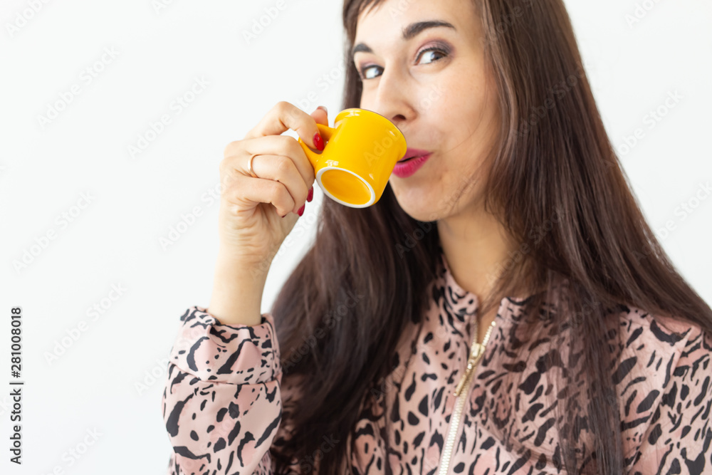 Cute young woman holding a small toy yellow mug in her hands posing on a white background. Favorite drinks concept Cute young woman holding a small toy yellow mug in her hands posing on a white background. Favorite drinks concept