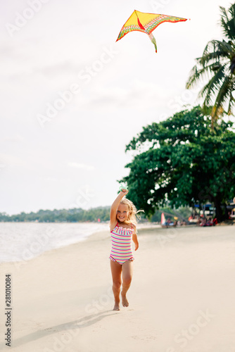 Happy pretty child girl with a kite running on tropical beach in summer