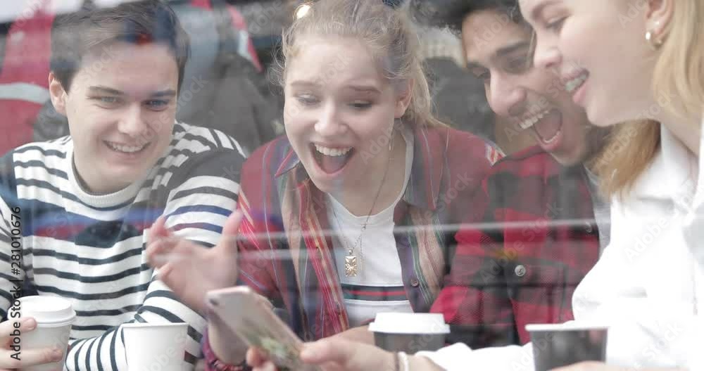 Happy multiracial friends looking at a smartphone in a cafe and laughing. Group of mixed race teenagers having fun together, sharing stories on social media and enjoying a coffee Happy multiracial friends looking at a smartphone in a cafe and laughing. Group of mixed race teenagers having fun together, sharing stories on social media and enjoying a coffee